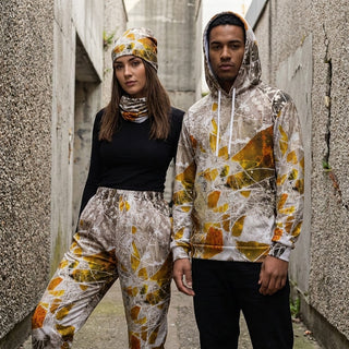 ERDGEWEBE Unisex-Trainingshose von REBL ART, Frau mit Mütze und Mann an der Betonwand