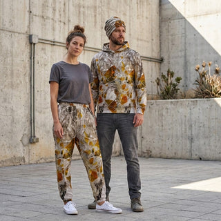 ERDGEWEBE Unisex-Trainingshose von REBL ART, Frau und Mann vor Betonmauer mit Pflanzen